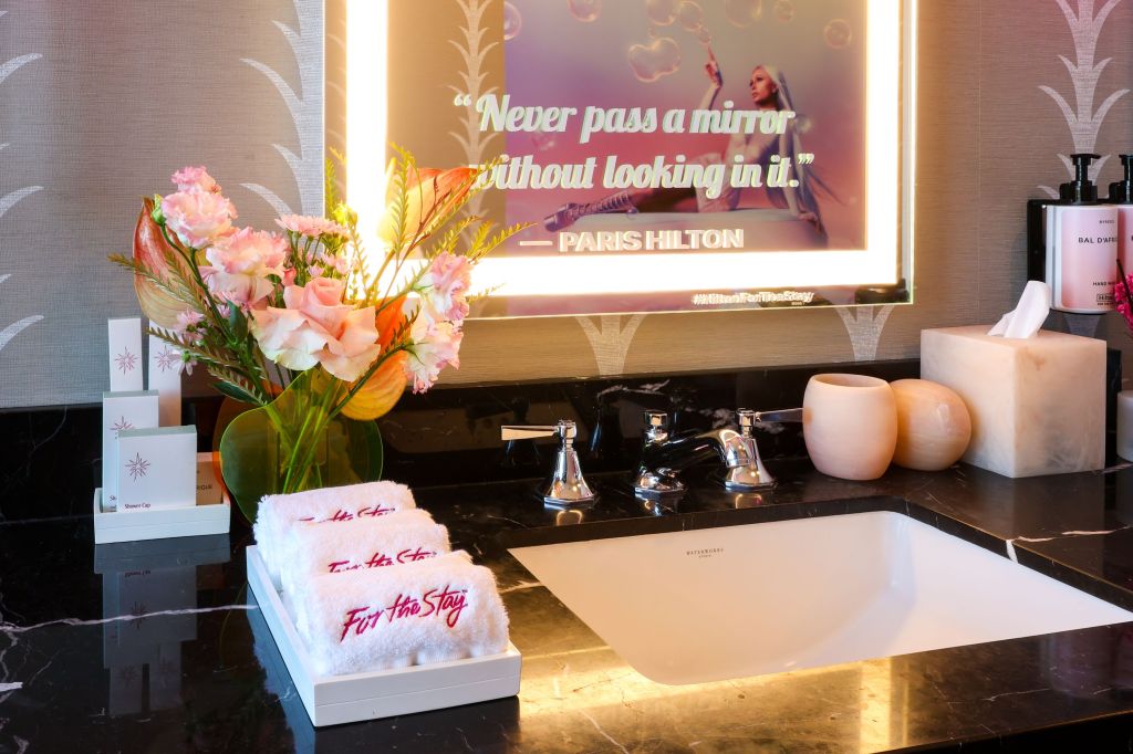 Stay Like an Infinite Icon Themed Suites at Beverly Hilton - Spa-Like Bathroom Amenities include white towels with Pink For The Stay stitching, a mirror with Paris Hilton quote, &quot;Never pass a mirror without looking in it&quot;, pink flowers and pink hand wash and lotion - Credit Rich Polk Getty Images for Hilton