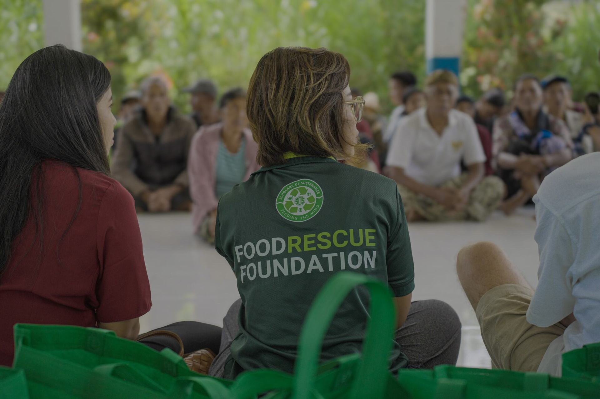 Scholars of Sustenance - Kuala Lumpur, Malaysia - Group of people sitting on the ground in a meeting, the back of a woman's shirt reads "Food Rescue Foundation"