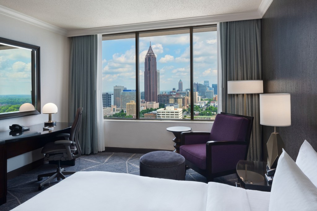 Hilton Atlanta King Guest Room - king bed with white bedding, purple chair, desk with large mirror and window overlooking the Atlanta skyline