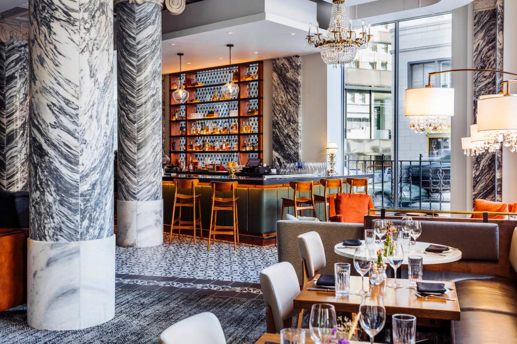 The Candler Hotel Atlanta, Curio Collection by Hilton - By George restaurant with black and white columns, tables and chairs and a colorful bar area and large window looking out to the street