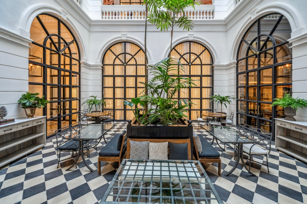 Palmaroga Hotel Asuncion, Tapestry Collection by Hilton, Patio, black framed arched windows, potted plants, courtyard, seating area, glass table top, outdoor furniture, diamond pattern flooring, checkerboard tiled floor, black seat cushions, wooden bench