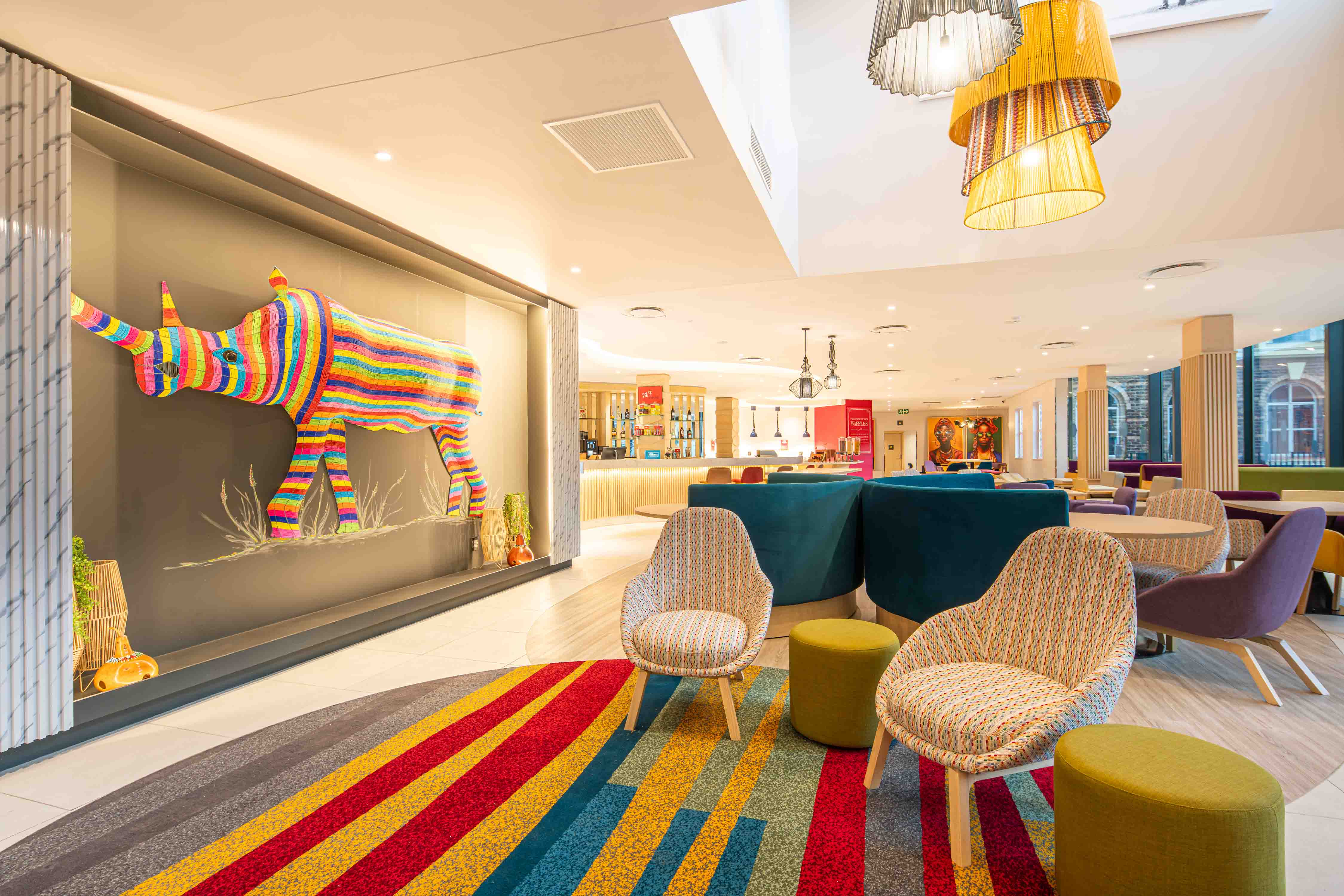 Hampton by Hilton Sandton Grayston - Lobby, multicolored chairs and ottomans, multicolored rhino art piece, bar area in background
