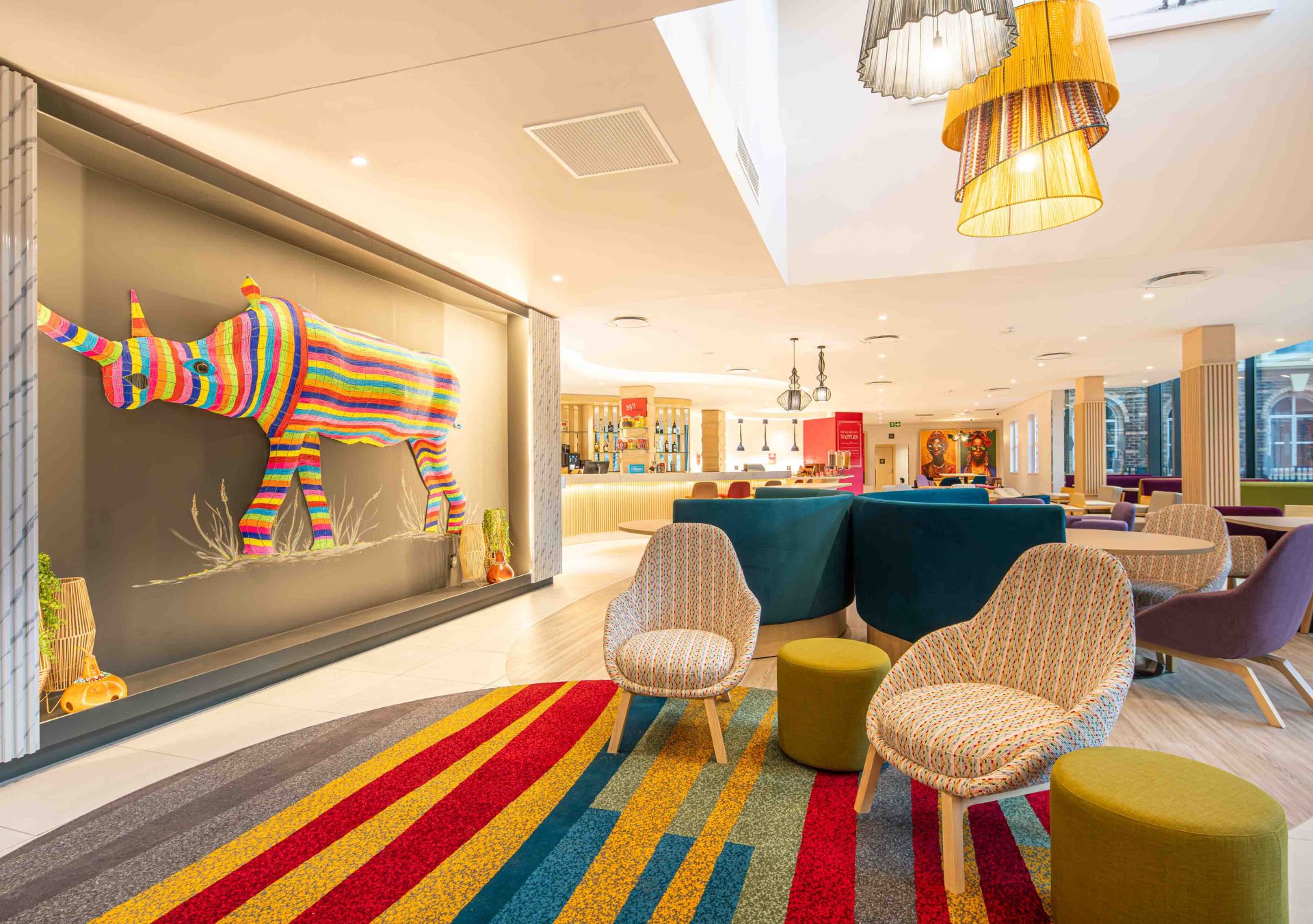 Hampton by Hilton Sandton Grayston - Lobby, multicolored chairs and ottomans, multicolored rhino art piece, bar area in background