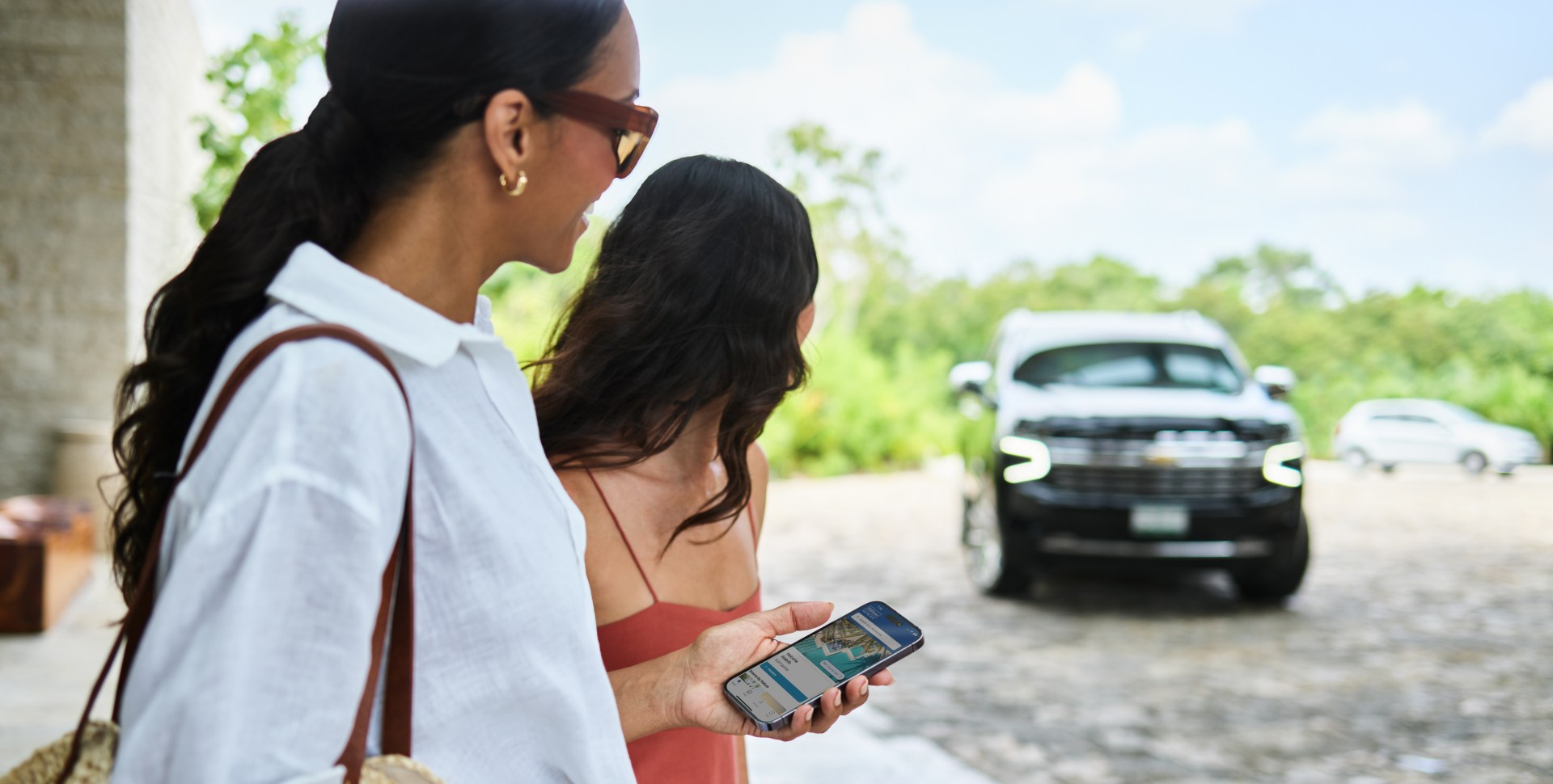 two women waiting for a car, one holding phone with Hilton Honors app open