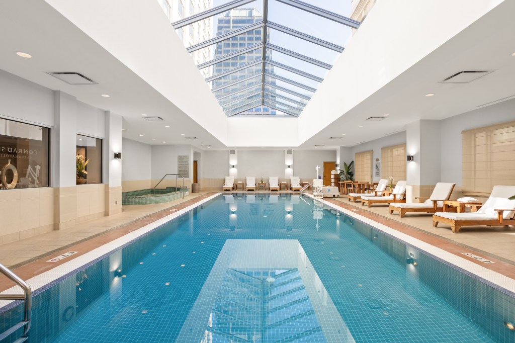 Conrad Indianapolis, Indoor Pool, skylight, white cushion chaise seating, blue tiled floor, plunge pool, wooden tables