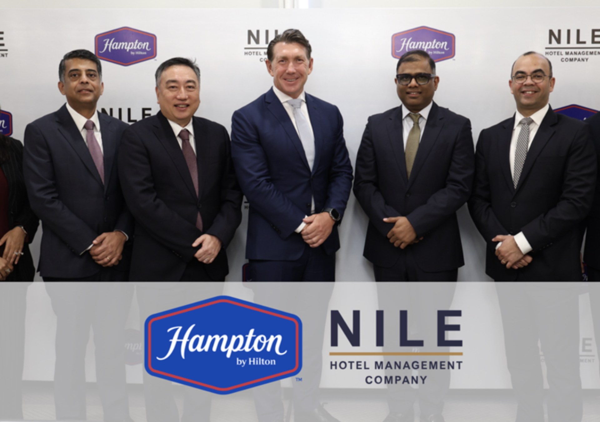 people standing and smiling in front of Hampton and NILE Hotel Management Company logo backdrop at the Hampton by Hilton and NILE Hospitality Signing Ceremony