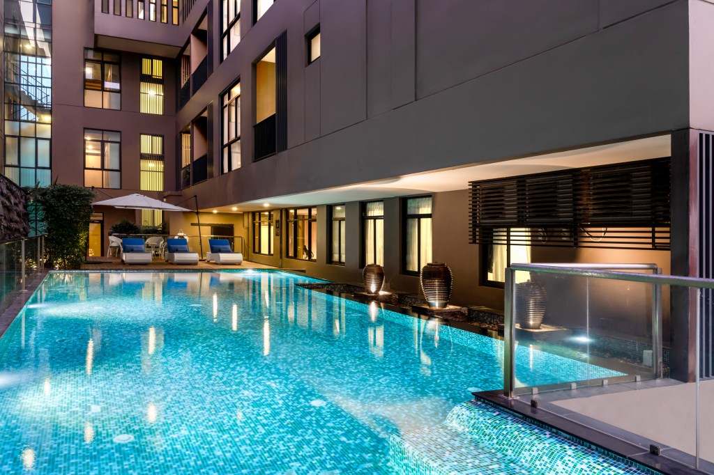 Metropolis Suites Bangkok, Tapestry Collection by Hilton, Pool, blue lounge chairs, umbrella, glass railing, tiled pool floor