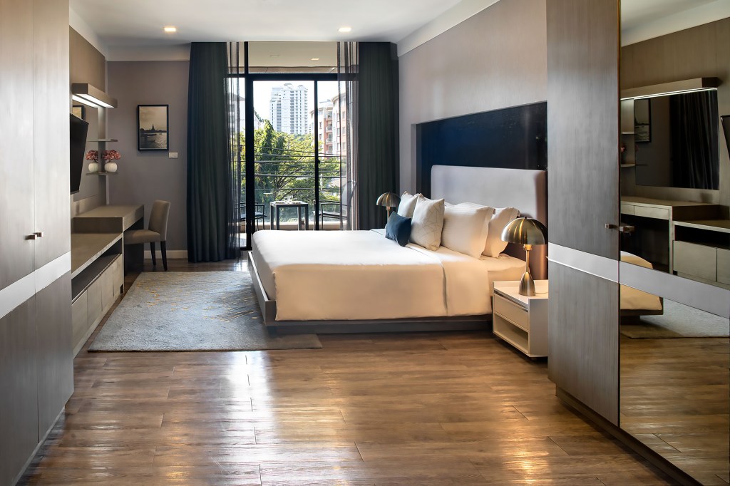 Metropolis Suites Bangkok, Tapestry Collection by Hilton, Suite, mirror, bedroom, desk chair, hanging artwork, brass table lamps, balcony seating