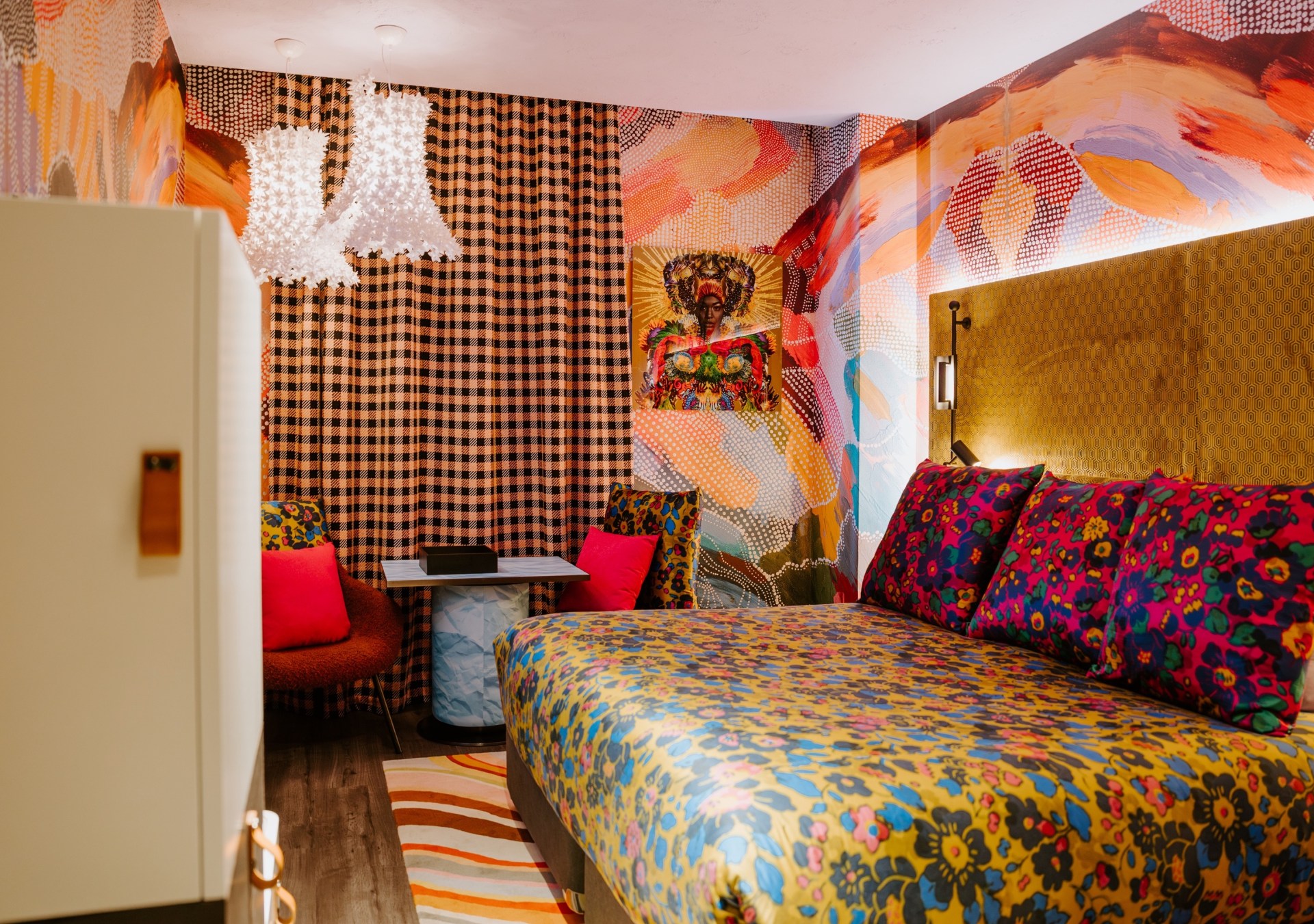 The Motley Hotel Richmond, Tapestry Collection by Hilton, Room, floral blanket, floral print, floral print throw pillows, white hanging light fixtures, colorful wall design, hanging artwork, red accent pillows, sitting area