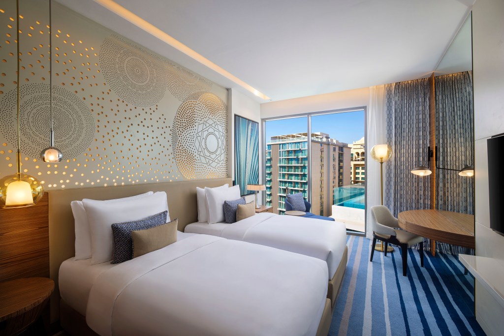 Tumbi West Palm Beach Hotel Dubai, Tapestry Collection by Hilton, Room, wall art, sitting area, wooden table, decorative lighting, framed artwork, white bedding, glass pendant light fixture, glass floor lamp, wooden nightstand, night light