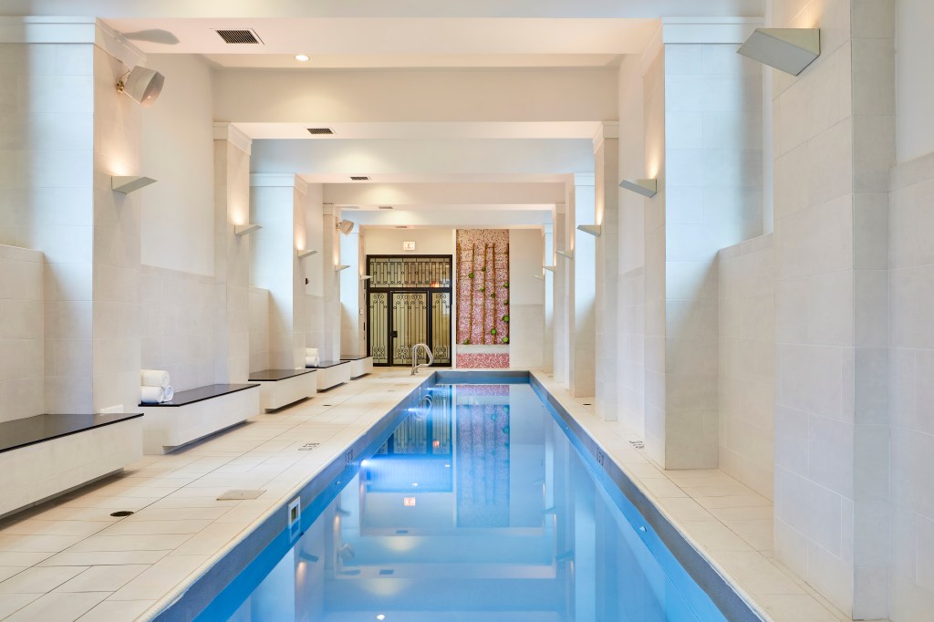 Waldorf Astoria Chicago, Indoor Pool, red design accent wall, bench seating, rolled white towels, blue tiled pool, sconce light fixtures, black framed entrance door