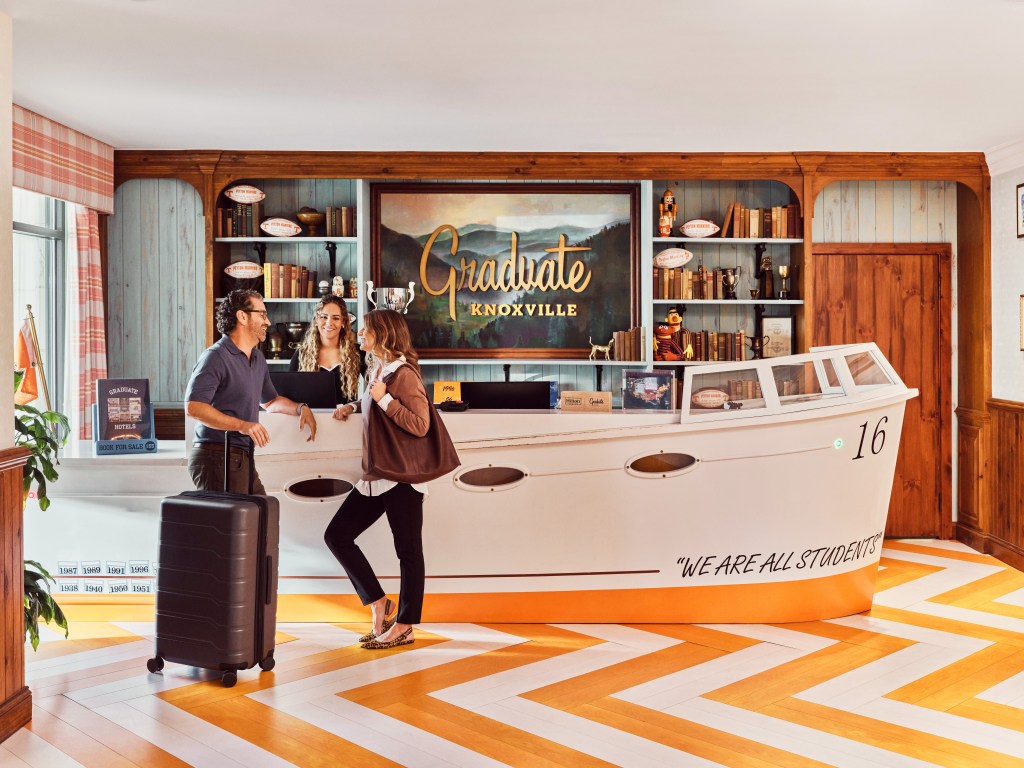 Graduate by Hilton Knoxville, orange and white zig zag design floor, boat shaped front lobby counter, bookshelf, suitcase, luggage, people talking at counter