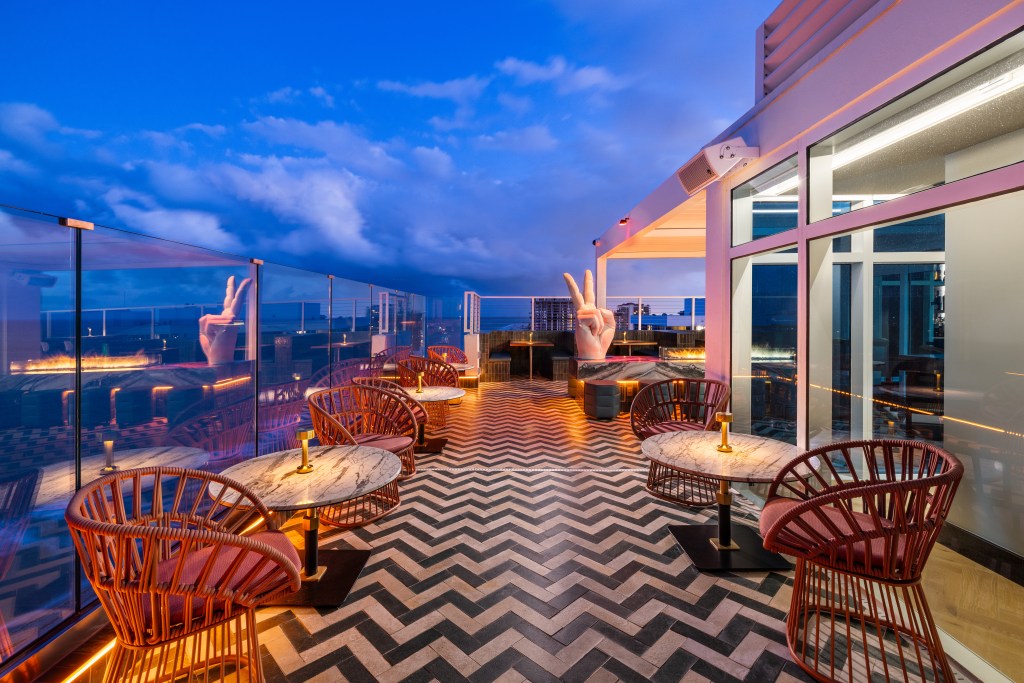 Beach House Fort Lauderdale, a Hilton Resort - Nubé Rooftop - wicker chairs and tables with decorative flor and statue of a hand giving a peace sign