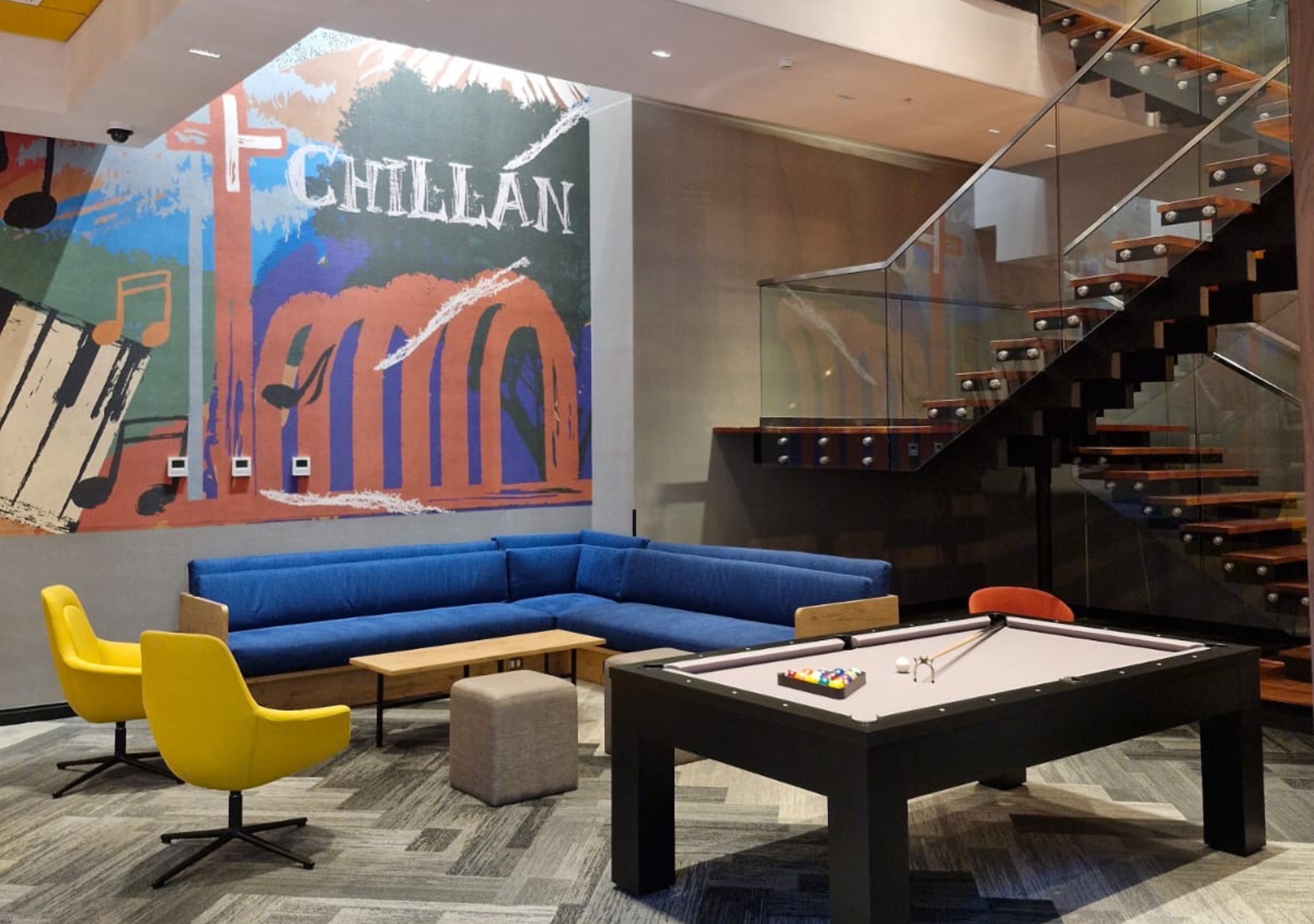 Tru by Hilton Chillan Ferrat Lobby, large wall mural with local art, blue couch, yellow chairs, pool table, staircase