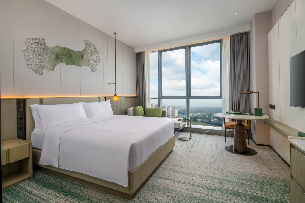 DoubleTree by Hilton Guang'an, Superior Room King, wall art with green accent color, bedroom with green accent color within the rug and the couch pillows and base of the table lamp as well as green stripes on the bed headboard. Bedroom with window view of the city