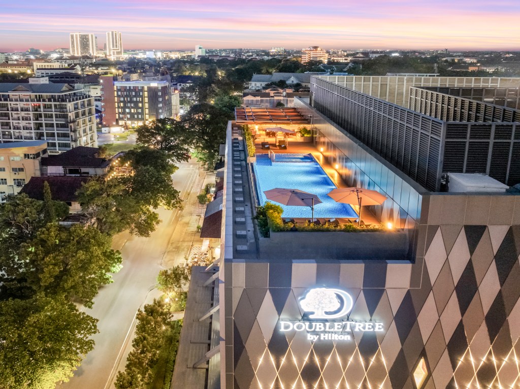 DoubleTree by Hilton Vientiane exterior of building with sign lit up, Rooftop Bar and Swimming Pool overlooking the city and tree lined street