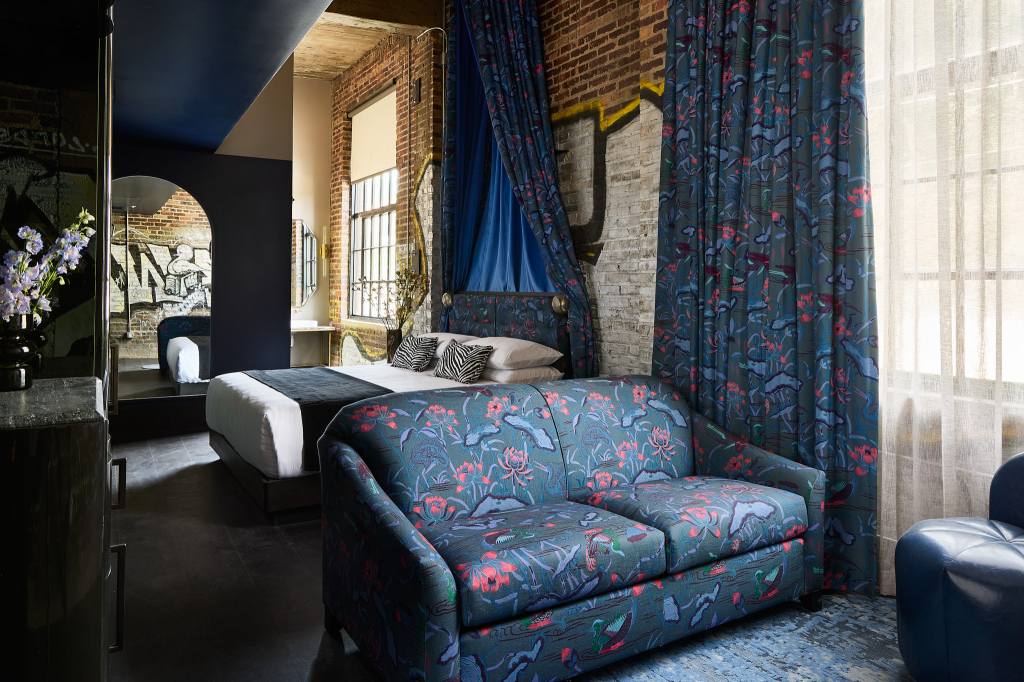Guest suite with love seat couch next to bed with zebra print accent pillows on it next to bathroom entrance and a large mirror and exposed brick walls, matching fabric on couch and headboard and curtains