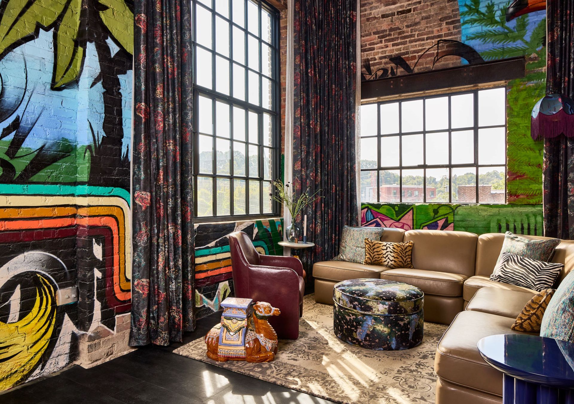 Lobby with painted brick wall and leather chair and l-shaped couch with throw pillows next to an ottoman and end tables all sitting on top of a patterned rug
