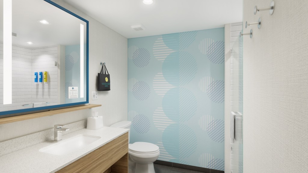 Tru by Hilton, Bathroom, accent wall with tricolor circle design, blue framed mirror above bathroom vanity, wooden vanity