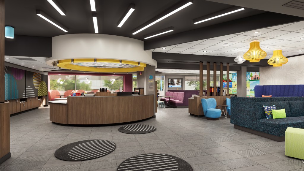Tru by Hilton, Entry with round rugs on the floor leading up to reception desk and a sitting area with tables with yellow and white light fixtures on the ceiling
