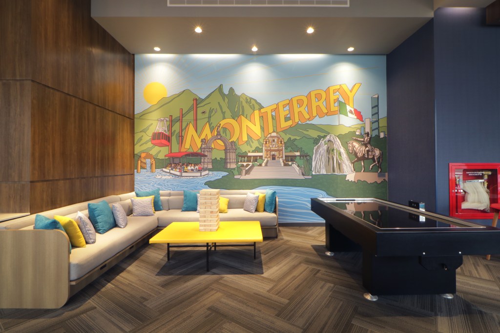 Tru by Hilton Monterrey Fundidora, mural wall art, yellow coffee table, air hockey table, jenga table game, couch with yellow and gray and blue throw pillows
