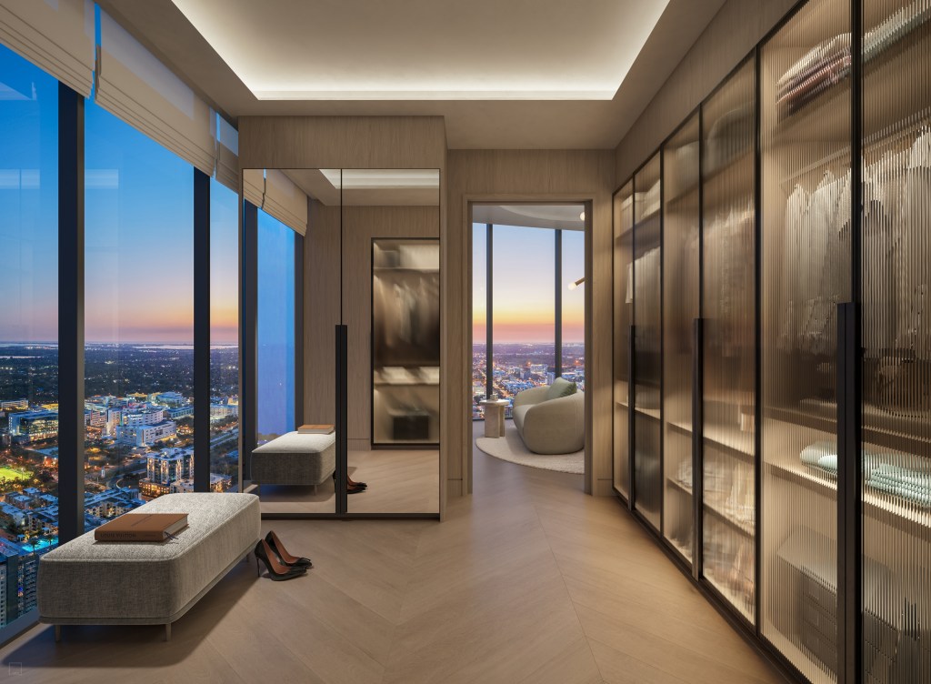 Primary closet with closets with glass doors and a bench next to windows overlooking city