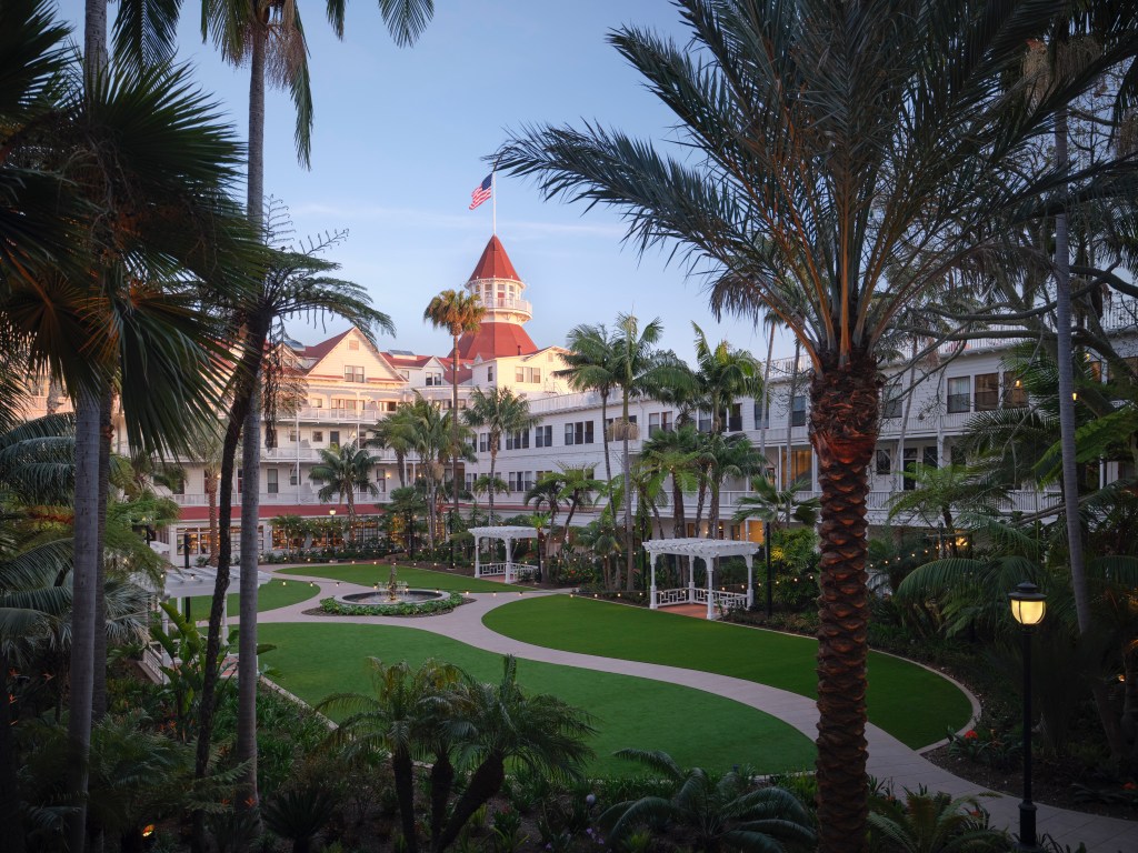 Victorian Garden at Sunset with twinkle lights hanging throughout the palm trees with a water fountain at the center of the walkways