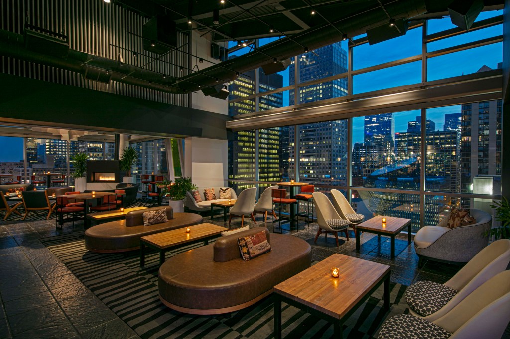 theWit Chicago a Hilton Hotel, seating area with multiple seating arrangements and candle lit lounge tables and a view of the city outside of the windows
