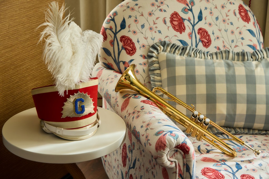 Graduate by Hilton Dallas Decor band hat laying on a white accent table and brass trumpet resting on a lounge chair with floral printed fabric and a throw pillow with white and blue gingham printed fabric
