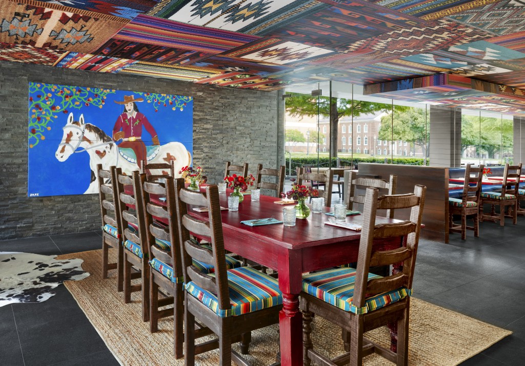 Graduate by Hilton Dallas, Los Charros Tex-Mex Smokehouse dining area with colorful ceiling and artwork on the wall as well as colorful dining chair cushions