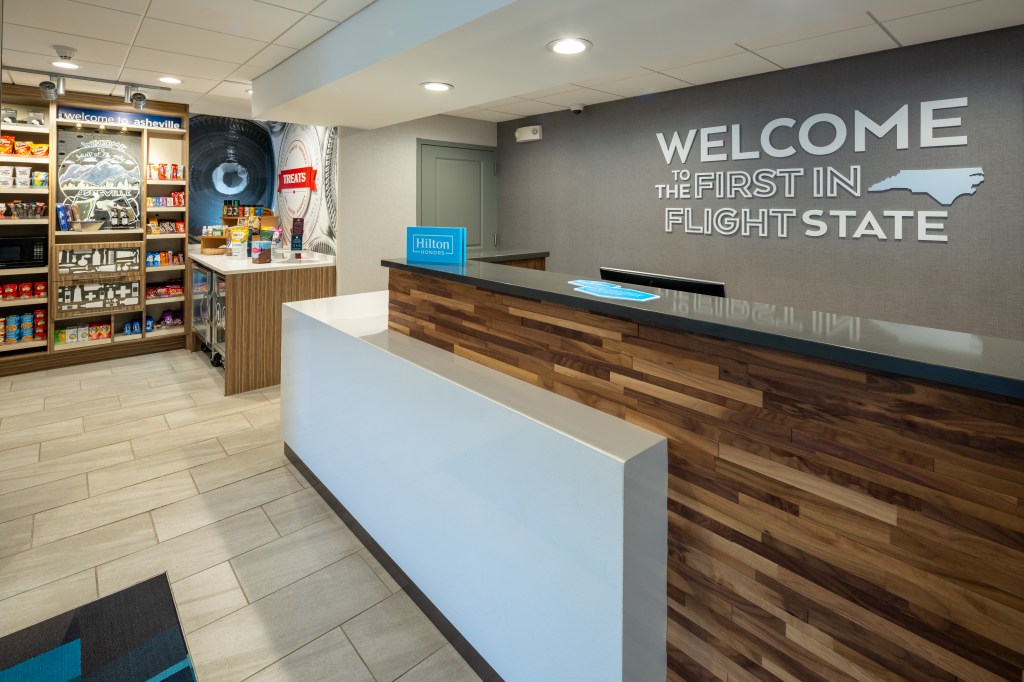 Hampton Inn Asheville-Tunnel Road - Front Desk with wall mural that says &quot;Welcome to the First in Flight State&quot;, shop with snacks to the left