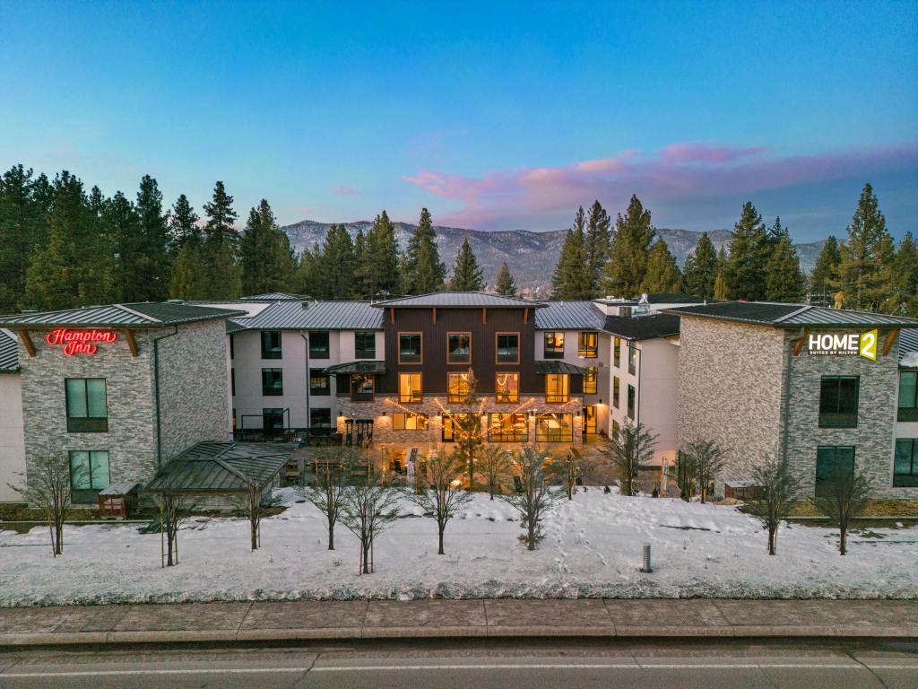 Hampton Inn Big Bear Lake - Exterior of hotel at dusk with blue sky and purple/pink clouds in the distance, snow on the ground and green trees surrounding the building