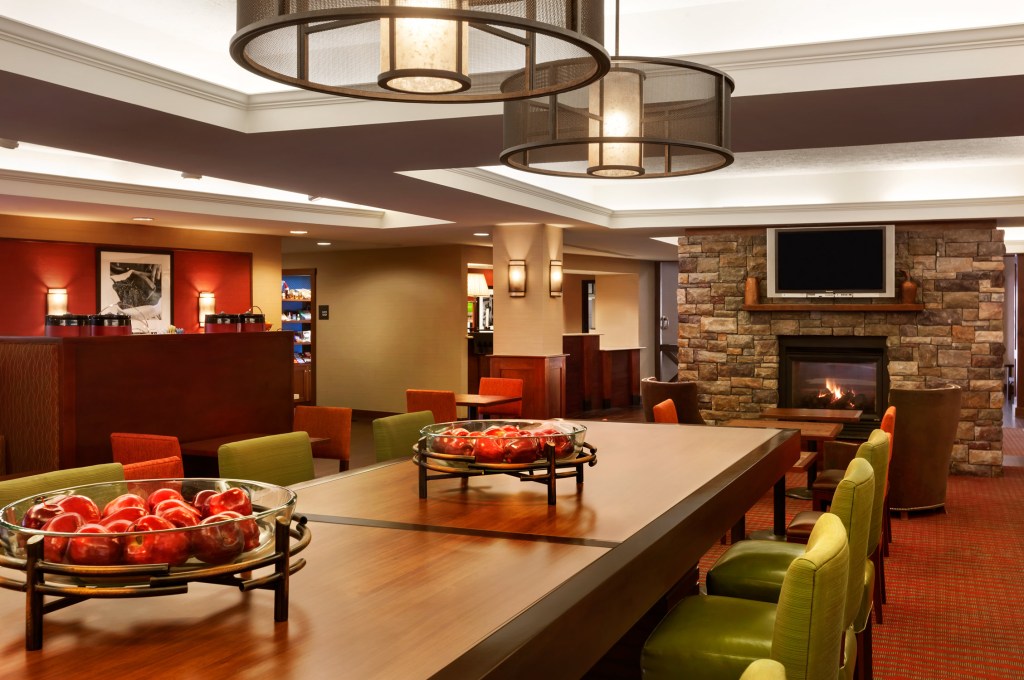 Hampton Inn Colchester - Lobby with large table, green chairs, seating area in front of a fireplace