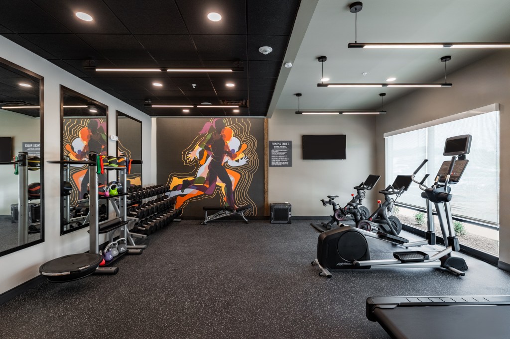 LivSmart Studios by Hilton Tullahoma - Gym with colorful mural wall, Peloton bikes, elliptical machine, treadmill and weights