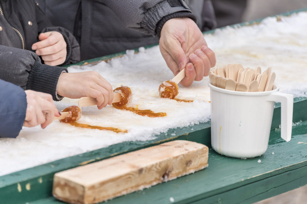 Hands rolling maple taffy on snow at a traditional sugar shack in Montreal, showcasing a beloved wintertime treat in Quebec.