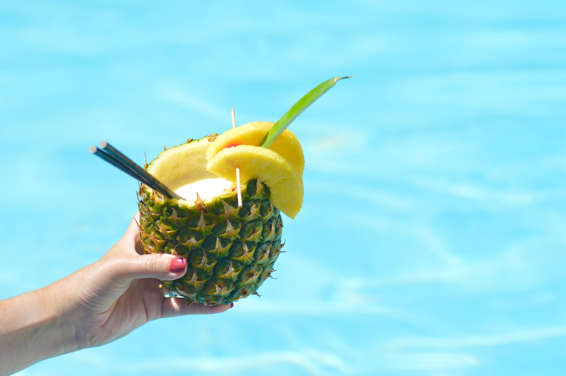 Hand holding piña colada cocktail made in a real pineapple at a Pool