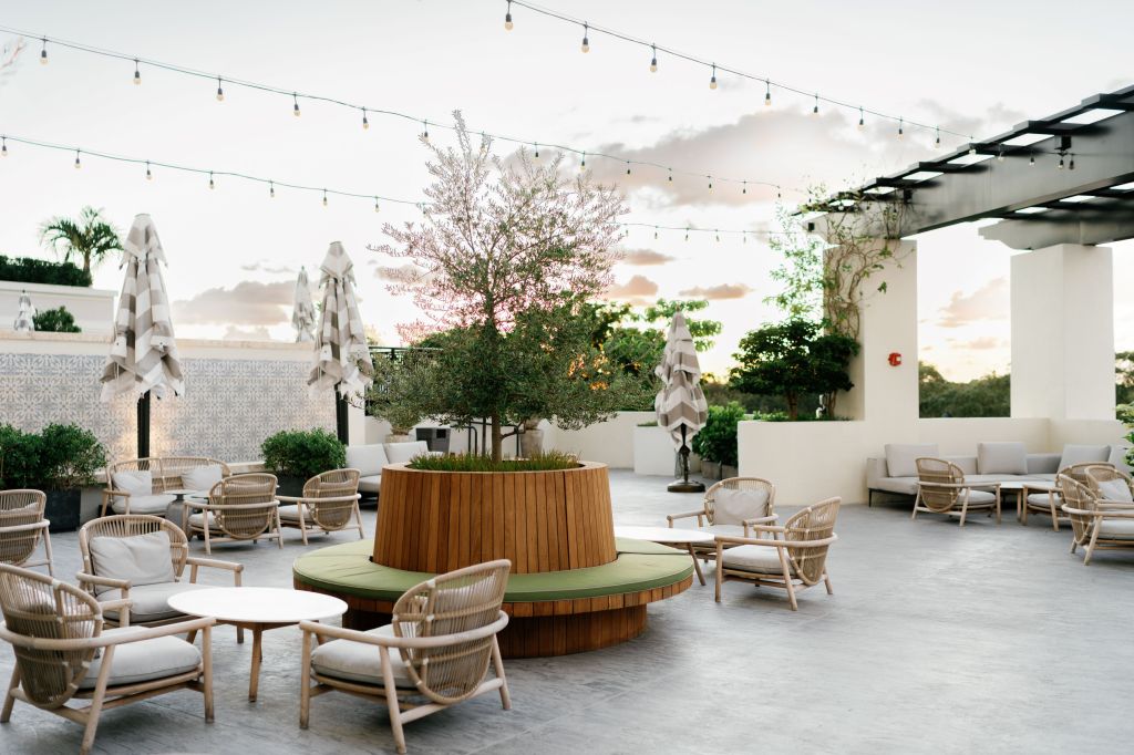 THesis Hotel Miami Coral Gables, Curio Collection by Hilton, outdoor patio seating area with variety of tables and chairs, overhead string lights, large circular planter with green cushions