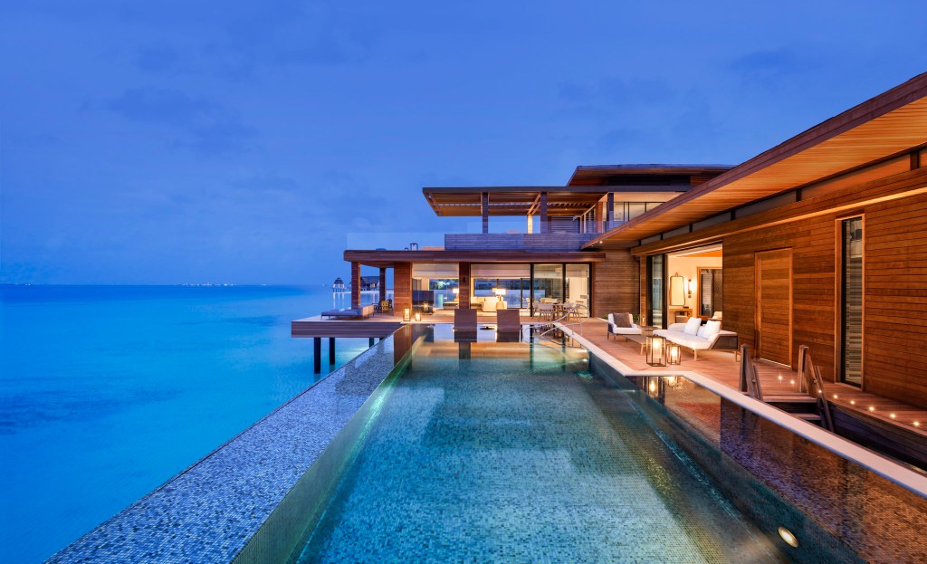 Private overwater villa with a shimmering infinity pool overlooking the calm turquoise ocean at twilight. Waldorf Astoria Maldives Ithaafushi, Pool at Twilight. Hilton