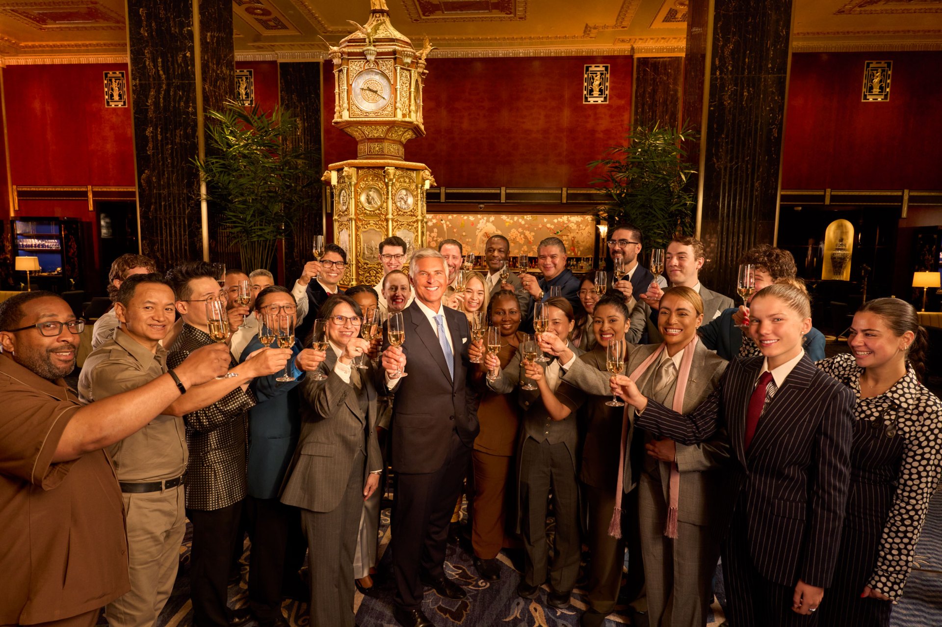 large group of Waldorf Astoria New York team members and Chris Nassetta, president and CEO, Hilton raise champagne glasses in Peacock Alley at Waldorf Astoria New York