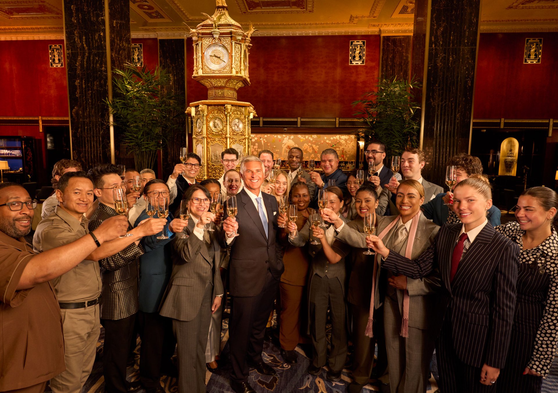 large group of Waldorf Astoria New York team members and Chris Nassetta, president and CEO, Hilton raise champagne glasses in Peacock Alley at Waldorf Astoria New York