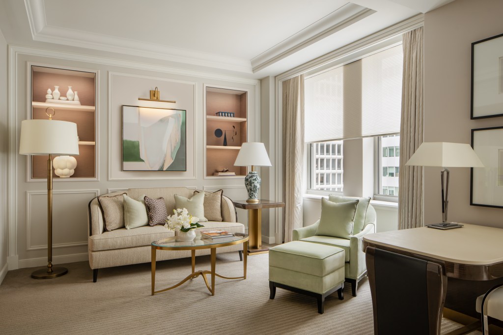 Waldorf Astoria New York Park Avenue Junior Suite Living Space with a art filled all displayed on nested shelves and under a picture light with a couch and lamps with a tables and a lounge chair in front of windows