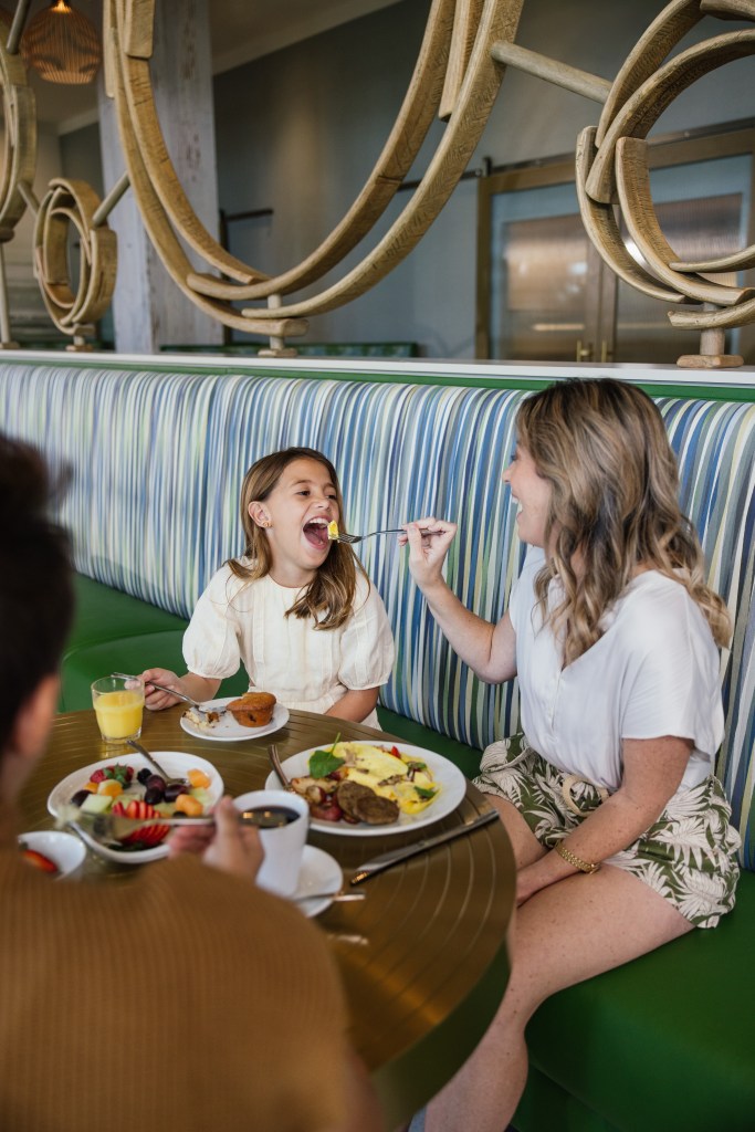 Embassy Suites by Hilton - Family Eating Breakfast, mother feeding her daughter a piece of her food