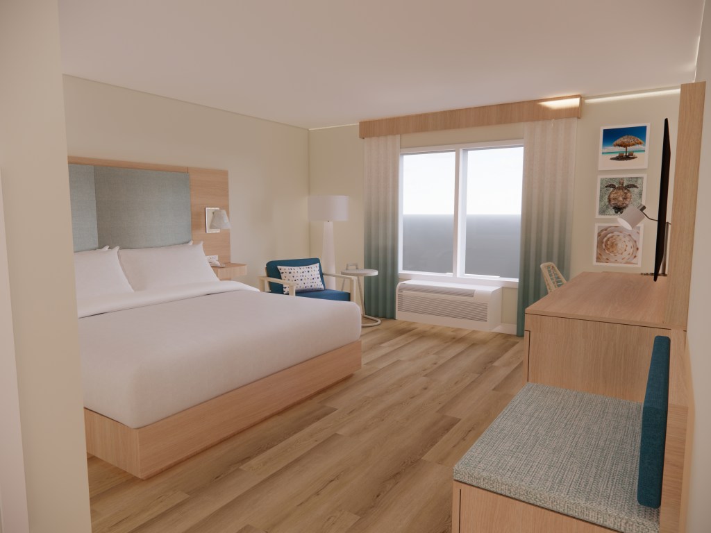 Hampton by Hilton St. Thomas Guest Room with a bed next to a lounge chair with a floor lamp and table next to a window facing a desk with chair next to three framed photos hanging on the wall