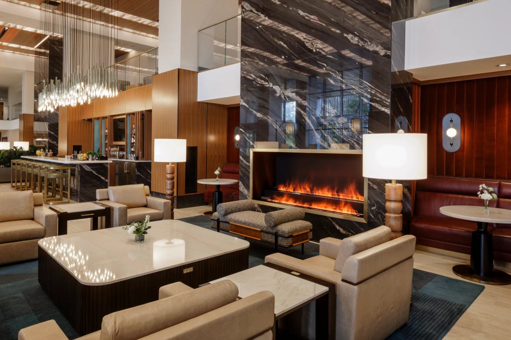 Hilton Arlington Rosslyn The Key Lobby Fireplace Seating Area with marble top tables wooden floor lamps and a fireplace and a bar with black marble and gold bar stools with cluster pendant lighting hung above