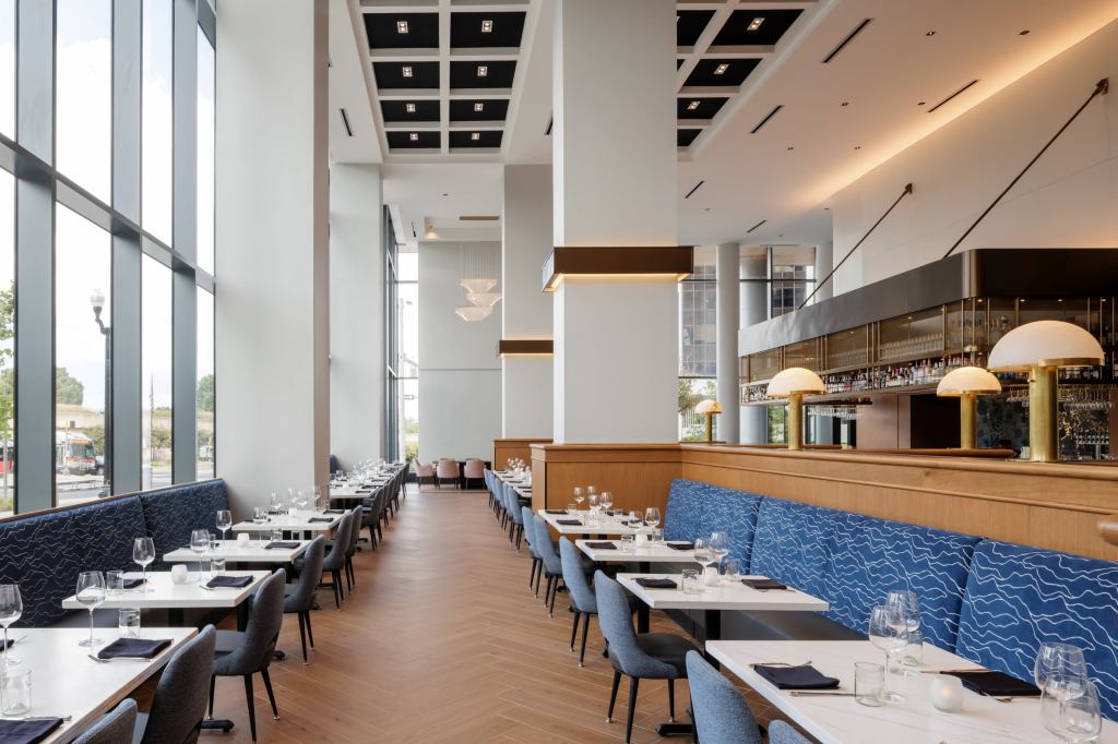 Hilton Arlington Rosslyn The Key Locket Restaurant dining room sitting area with blue print fabric cushioned bench seating and wood flooring and brass lamps mounted on top of wooden partitions