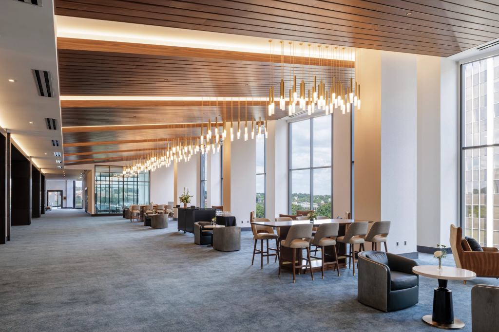 Hilton Arlington Rosslyn The Key Pre-Event Area with multiple lounge sitting areas with comfortable lounge seats with accent tables and high top tables with high backed stools in a room with wooden ceiling sections with cluster pendant light fixtures and a wall with floor to ceiling windows