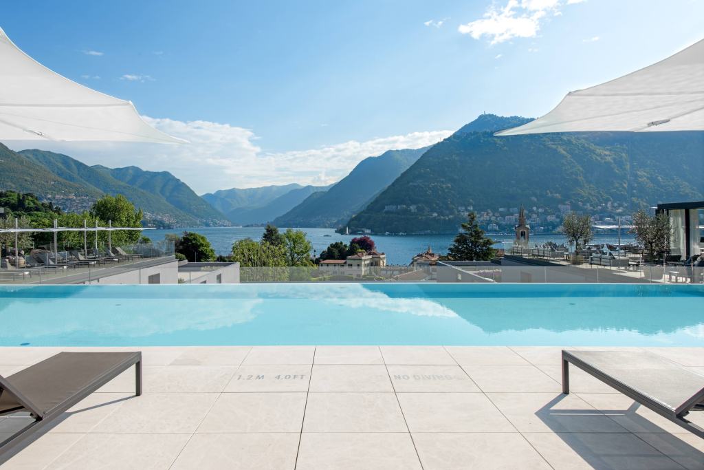 Hilton Lake Como Rooftop Pool with view of the lake and mountains, poolside lounge chairs and white umbrellas