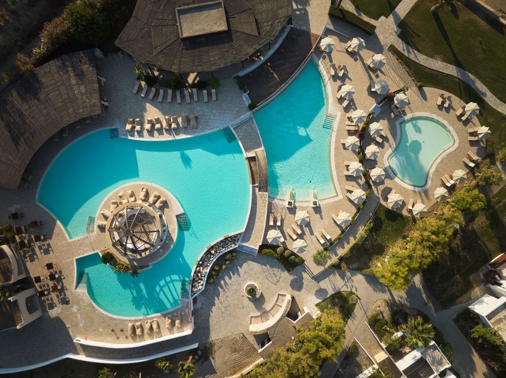 Lindian Village All-Inclusive Resort Rhodes, Curio Collection by Hilton Pool Aerial, poof chairs, pool lounge seating with umbrellas