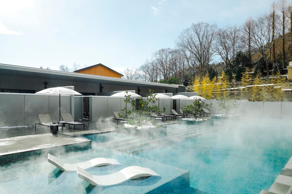 ROKU KYOTO, LXR Hotels &amp; Resorts Thermal Pool with potted trees and chaise pool lounge chairs and umbrella next to and lounge chaise chairs in the shallow end of the pool