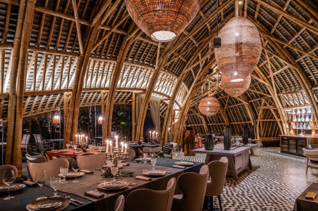 Sundy Praia an SLH Hotel (São Tomé and Principe) Restaurant indoor dining area within an eco-lodge adorned with light fixtures and domed ceiling using natural materials and dining tables with high back dining chairs on a black and white patterned flooring
